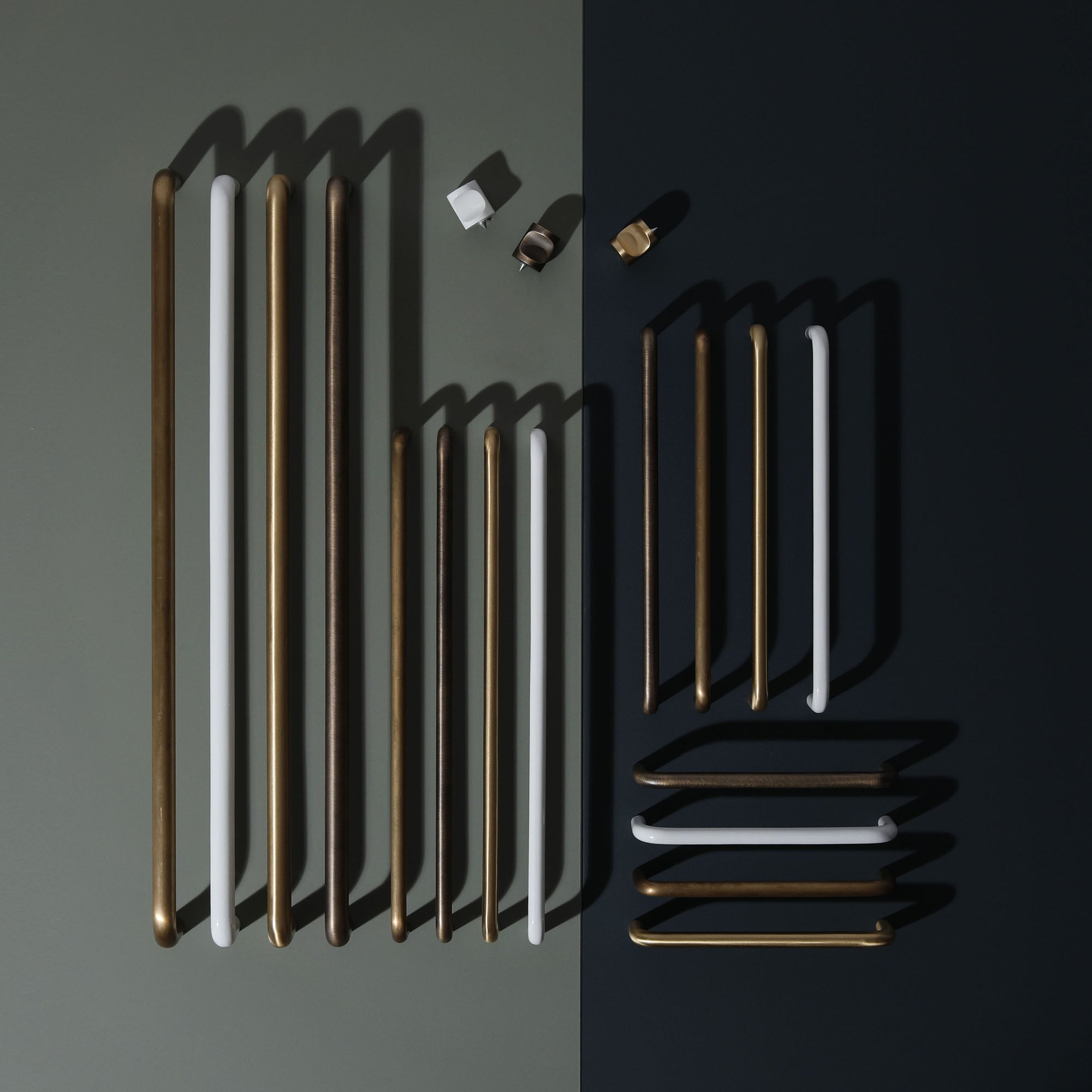 Assorted modern cabinet and door handles in brass, bronze, and white finishes displayed on a two-tone background – Ren Studio.