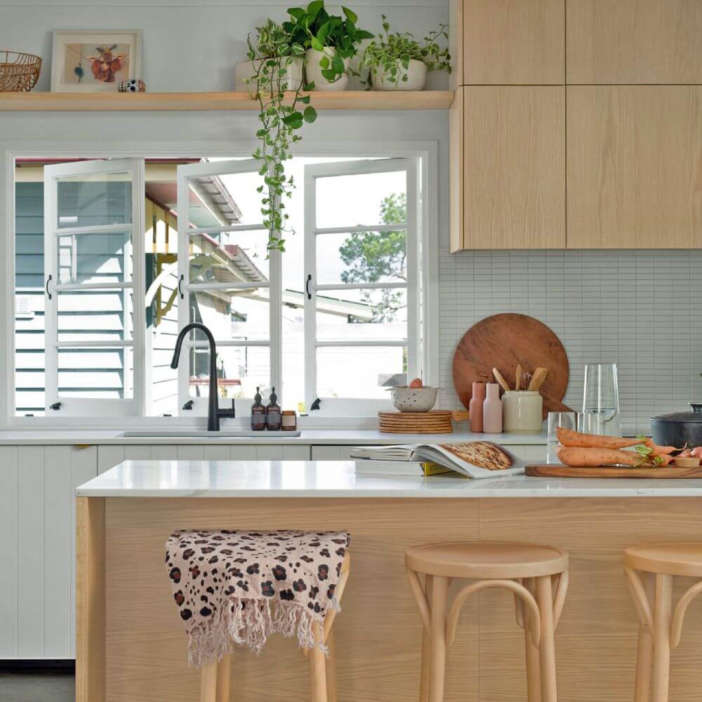 Bright kitchen with light wood cabinetry, white countertops, indoor plants, and bar stools at the island – Ren Studio.