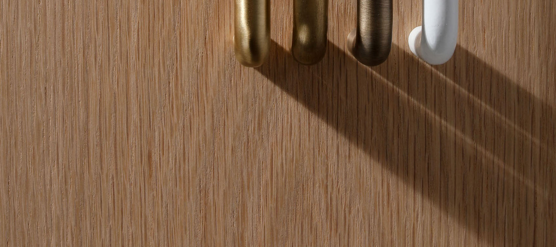 Close-up of brushed metal cabinet handles in gold, bronze, and white finishes on a natural timber surface, highlighting modern designer hardware.