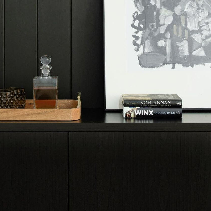 Black cabinetry with wooden tray, glass decanter, modern artwork, and white ceramic vases styled on a sleek sideboard – Ren Studio.