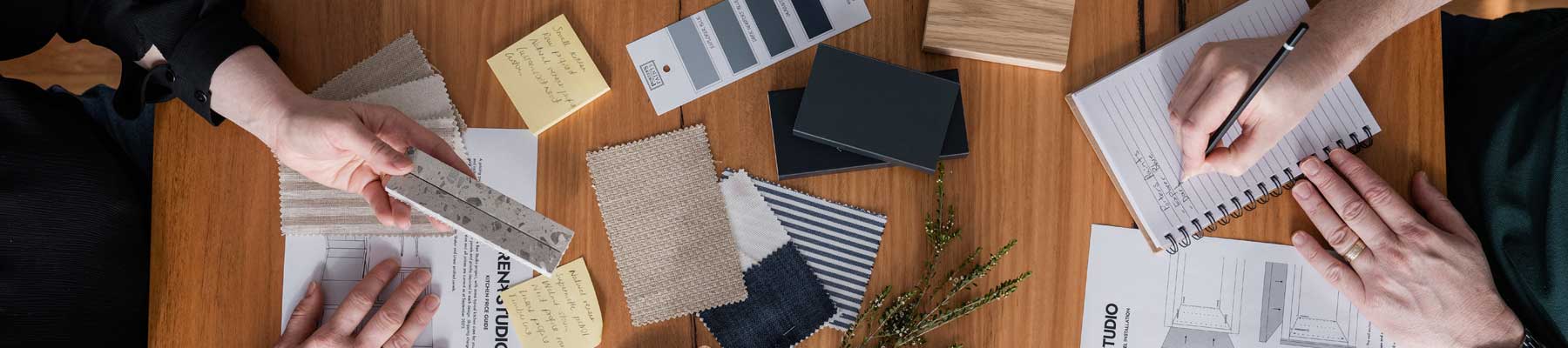 Interior designers reviewing material samples, paint swatches, and sketches on a wooden desk during a design consultation at REN Studio.