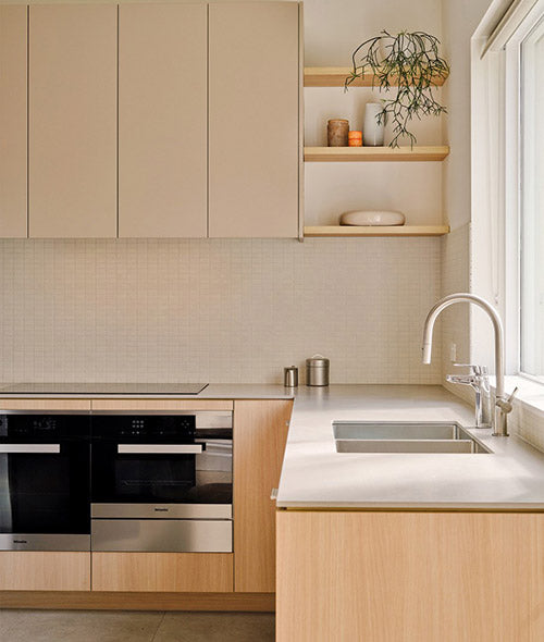 Modern minimalist kitchen with light wood cabinetry, built-in oven, open shelving, and large window for natural light – Ren Studio.