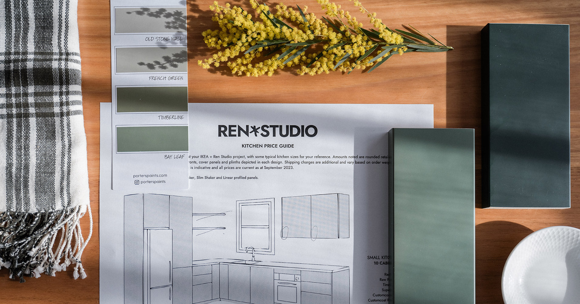 Ren Studio kitchen price guide with green paint swatches, fabric sample, and yellow floral accent on wooden table – Ren Studio.