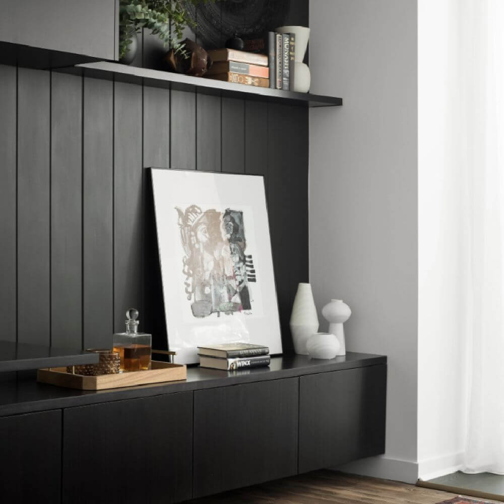Modern living space with black cabinetry, decorative artwork, books, and minimalist accessories against a dark feature wall – Ren Studio.