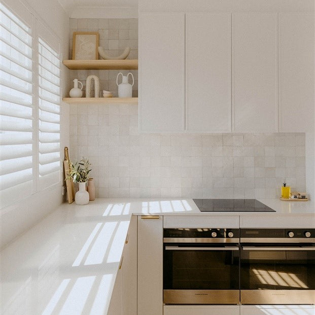 Bright minimalist kitchen with white cabinetry, tiled backsplash, built-in ovens, and open shelving decor – Ren Studio.