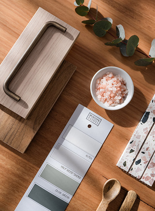 Flat lay of kitchen design samples with wood handle, paint swatches, terrazzo tile, pink salt, and wooden spoons on timber surface – Ren Studio.