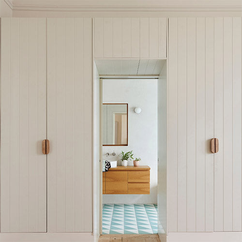 White panelled cabinetry with wooden handles leading to a modern bathroom.