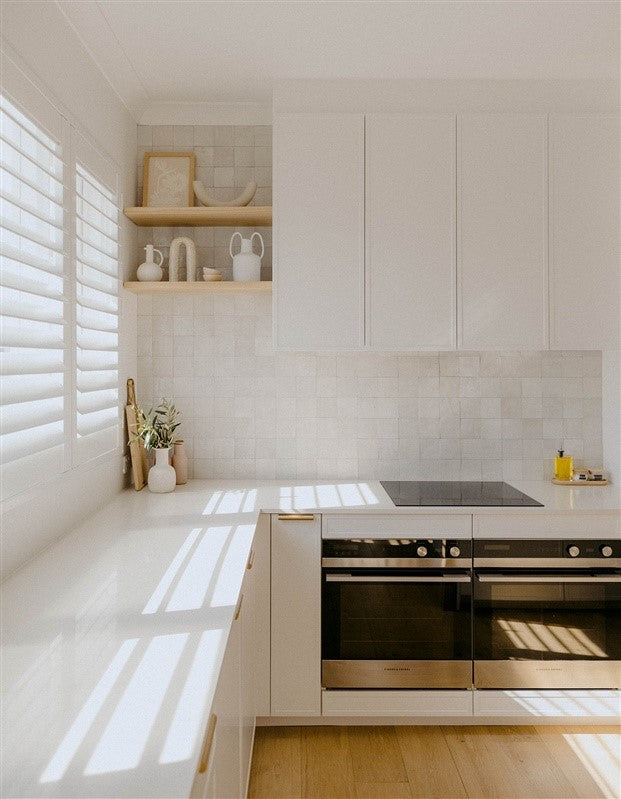Bright minimalist kitchen with white cabinetry, tiled backsplash, built-in ovens, and open shelving decor – Ren Studio.